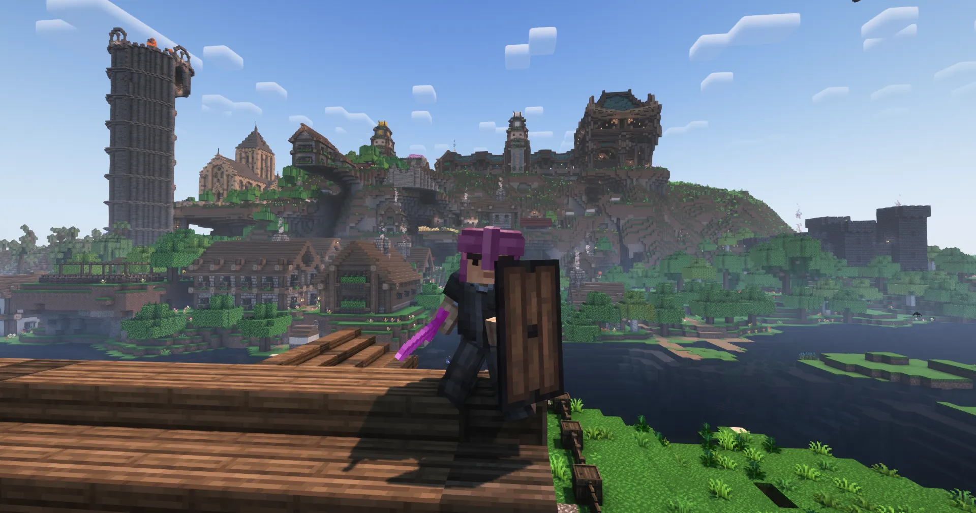 A player in dark armor holds a wooden shield on a pier, facing a hillside town of timber halls beside a tall stone tower
